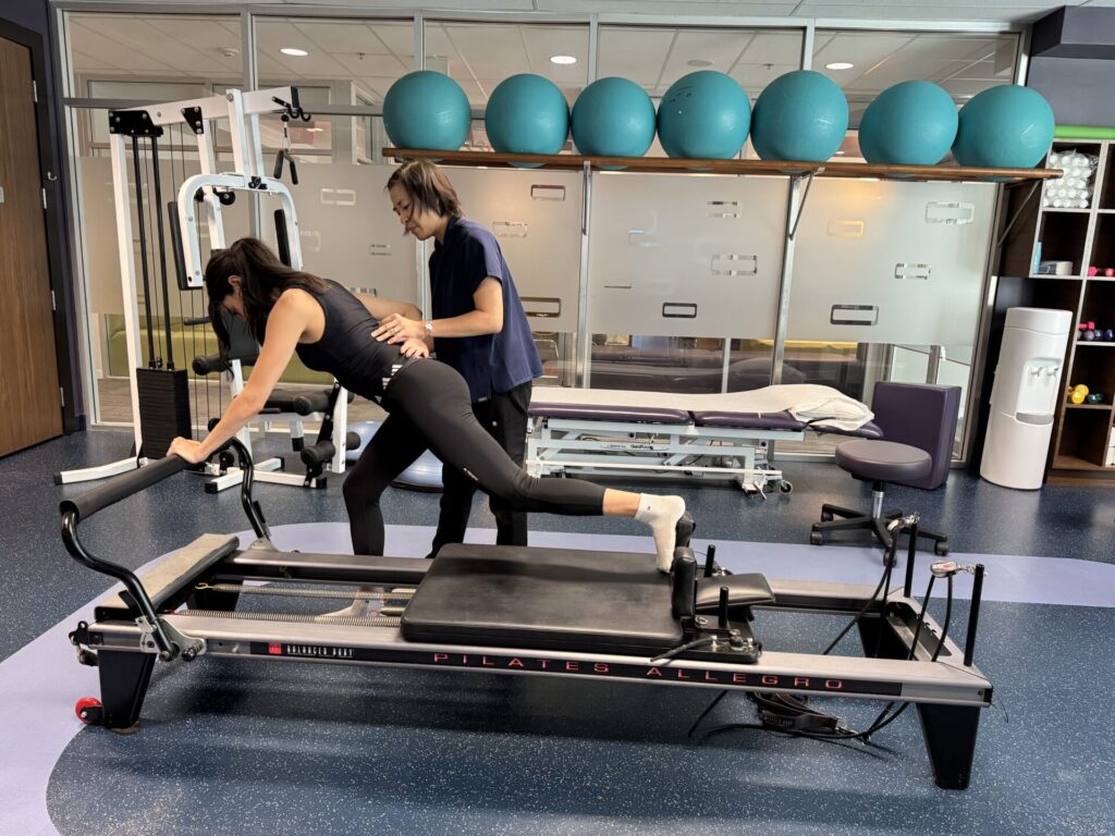 Vancouver physiotherapist Winnie Chan gives guidance to a patient on the reformer doing clinical pilates at Cross Roads Physiotherapy & Massage Therapy clinic