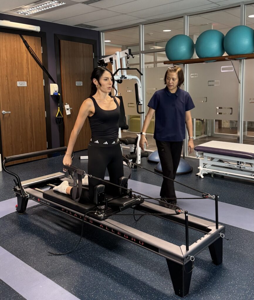 Vancouver physiotherapist Winnie Chan guides a patient doing clinical pilates exercises on a reformer unit at Cross Roads Physiotherapy & Massage Therapy clinic.