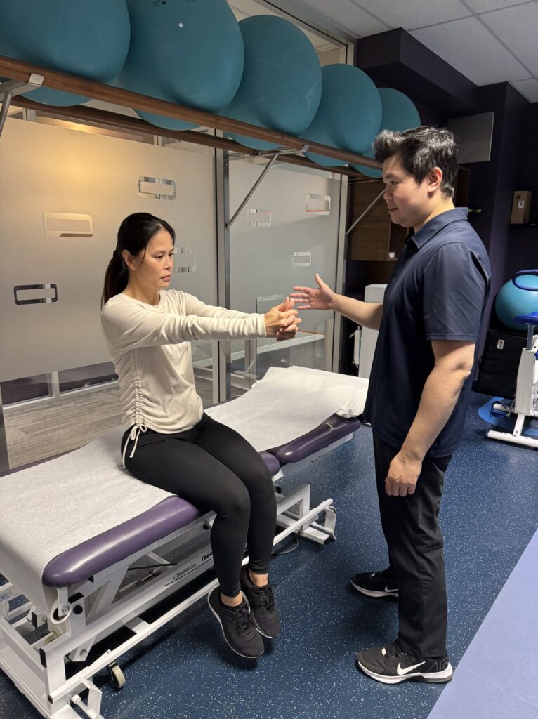 Vestibular physiotherapy in Vancouver at Cross Roads Physiotherapy & Massage Therapy clinic located on West Broadway at Cambie. Physiotherapist Jason is guiding a patient to do an exercise to train her eye gaze as she tracks her thumbs slowly moving left and right.